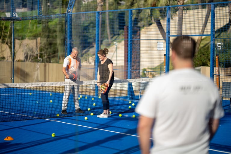 People playing paddle tennis on a blue court with a player in the foreground and others in the background behind the net